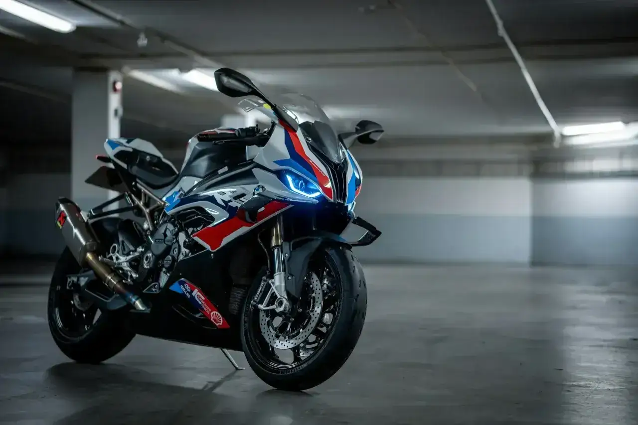 Sportowy motocykl BMW XR w biało-niebiesko-czerwonych barwach, z włączonymi światłami LED, zaparkowany w garażu.