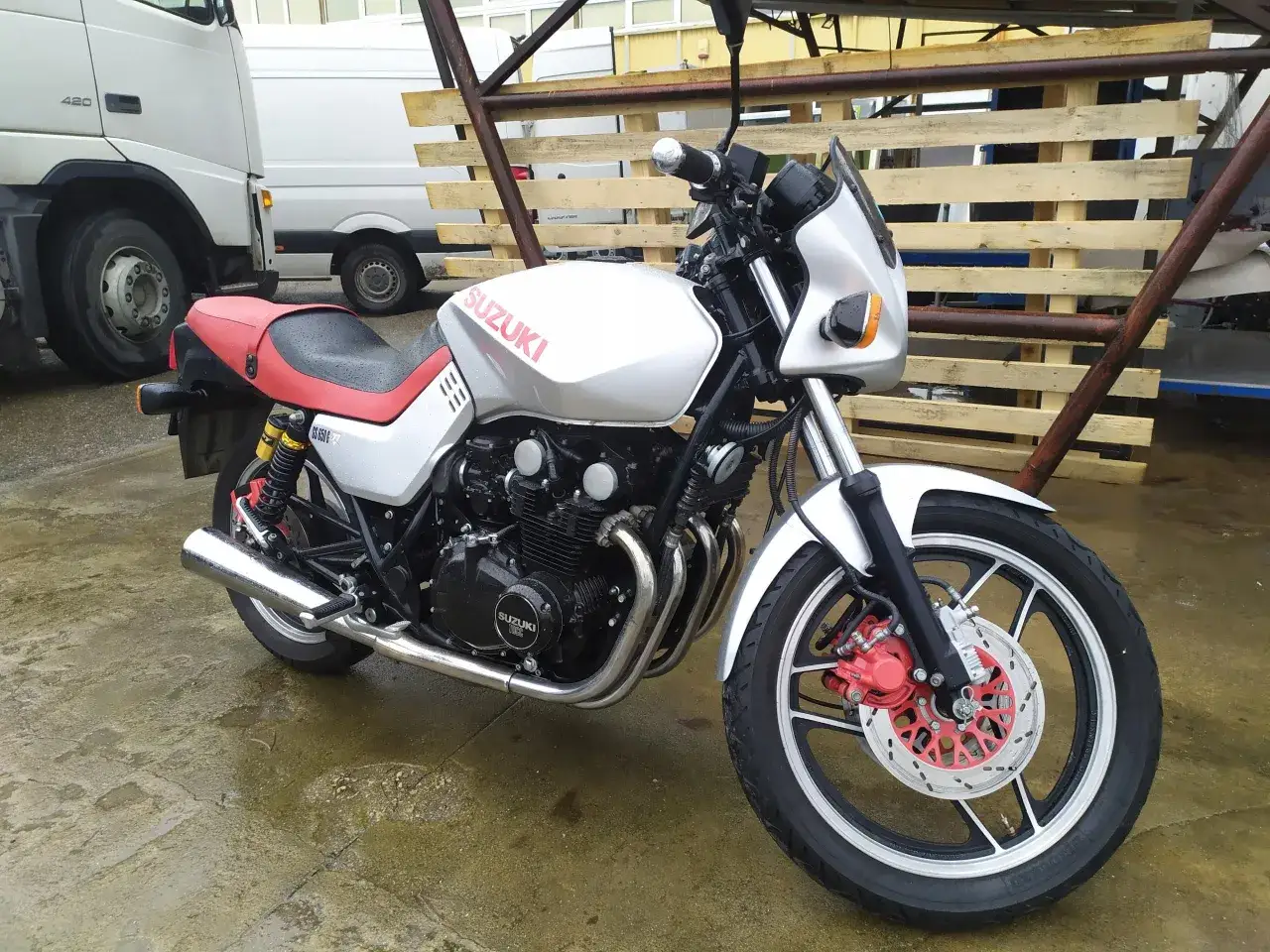 Srebrny motocykl Suzuki GS 650 z czerwoną kanapą stoi na mokrym asfalcie.