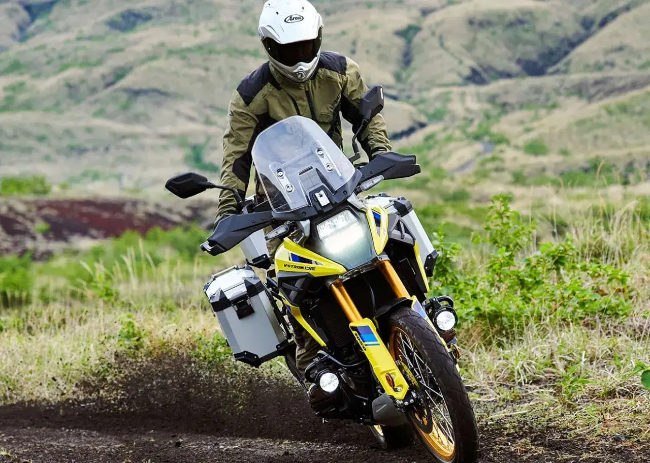 Motocyklista w kasku i kurtce jedzie żółtym motocyklem turystycznym po szutrowej drodze. To najlepszy motocykl turystyczny na przygodę.