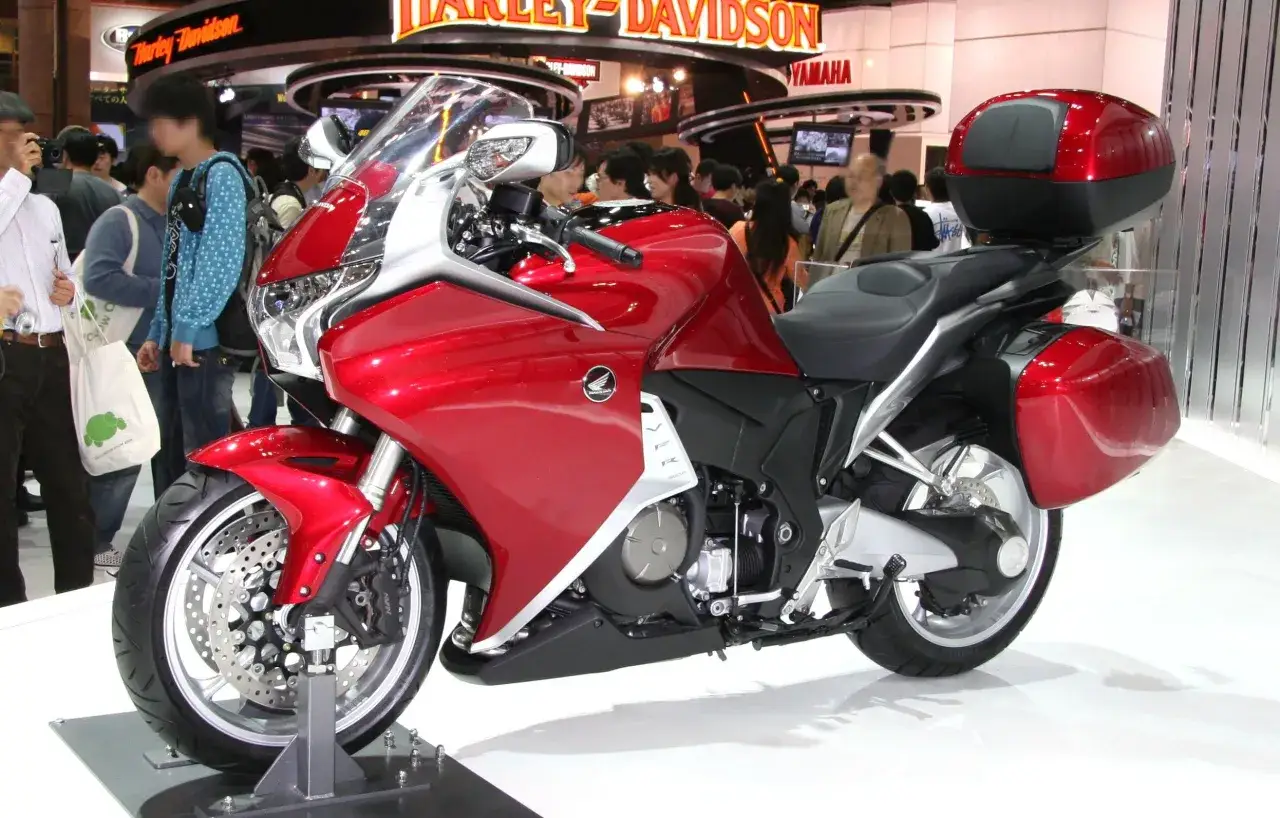 Czerwony motocykl Honda VFR 1200 z kuframi, prezentowany na wystawie motoryzacyjnej.