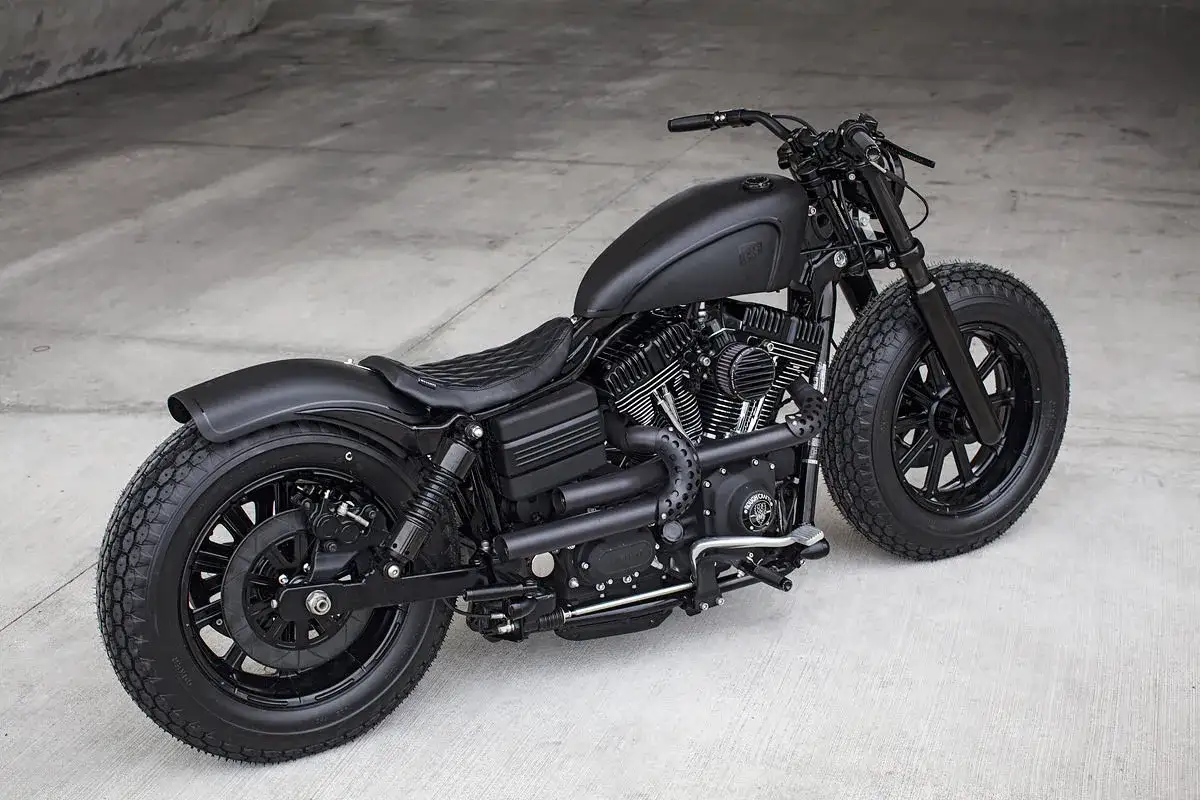 Czarny, customowy Harley Davidson Dyna z pikowanym siedzeniem i grubymi oponami, gotowy na drogę.