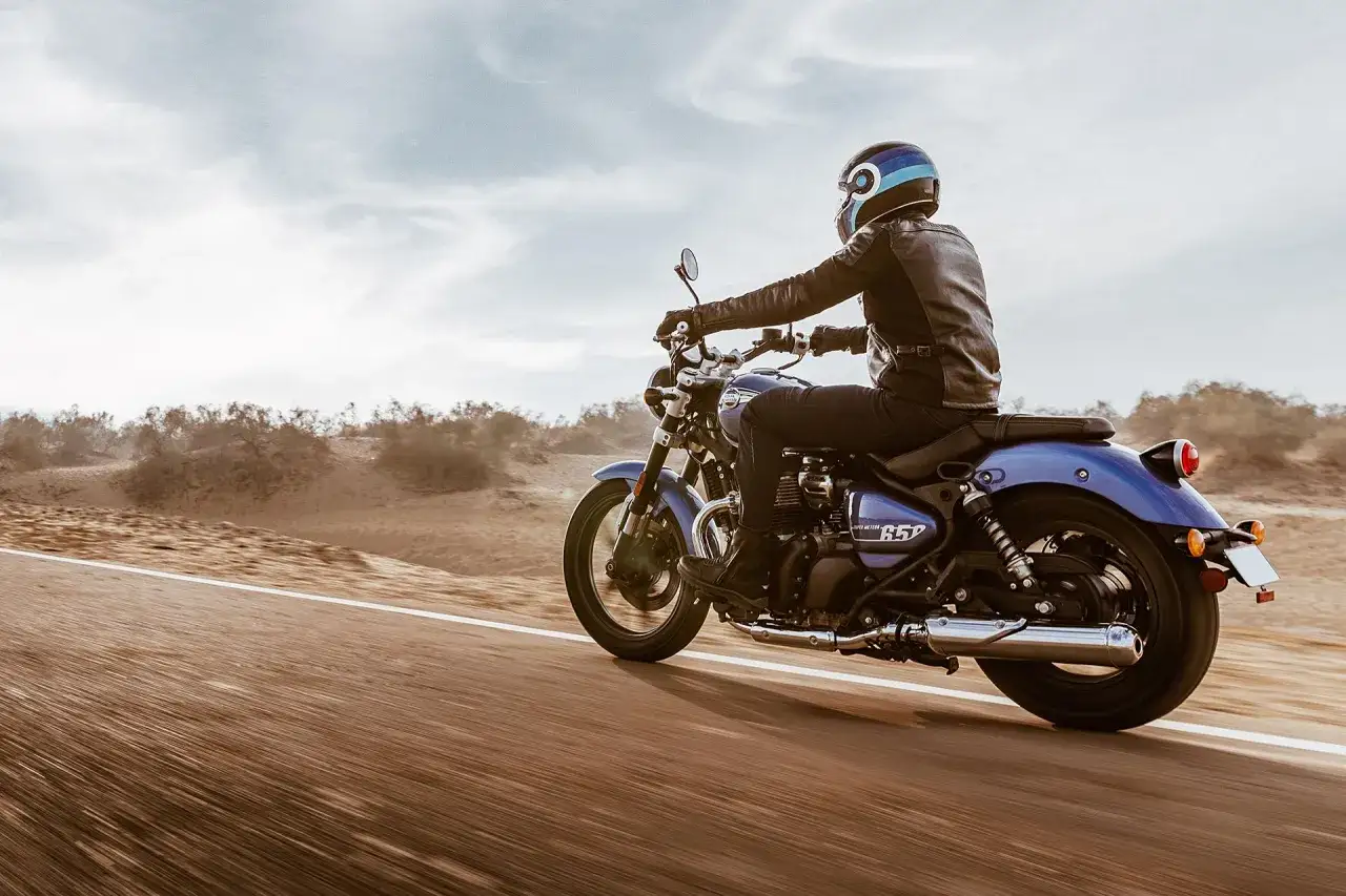 Jeździec w skórzanej kurtce pędzi na niebieskim Royal Enfield Meteor 650 przez pustynny krajobraz.