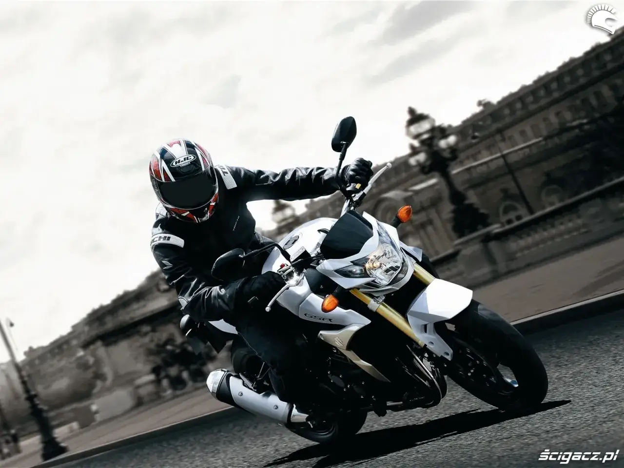 Motocyklista w kasku i skórze pochyla się na białym Suzuki GSR 750, pokonując zakręt. Nawet z potencjalnymi wadami, jazda nim to czysta przyjemność.