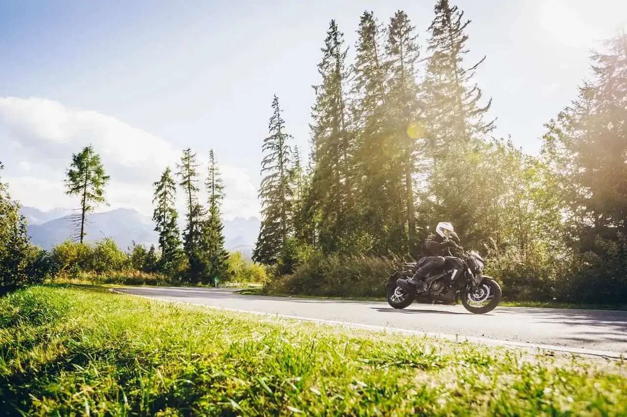 Motocyklista na Bajaj Dominar 400 przemierza malowniczą drogę wśród drzew i gór.