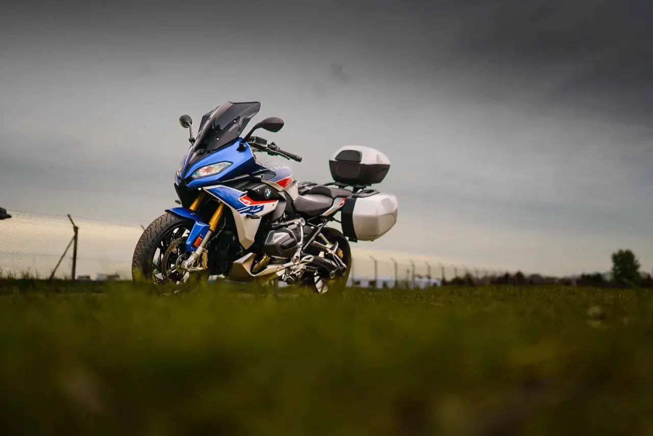 Niebiesko-biały motocykl BMW RS 1250 z kuframi, gotowy na przygodę na tle pochmurnego nieba.