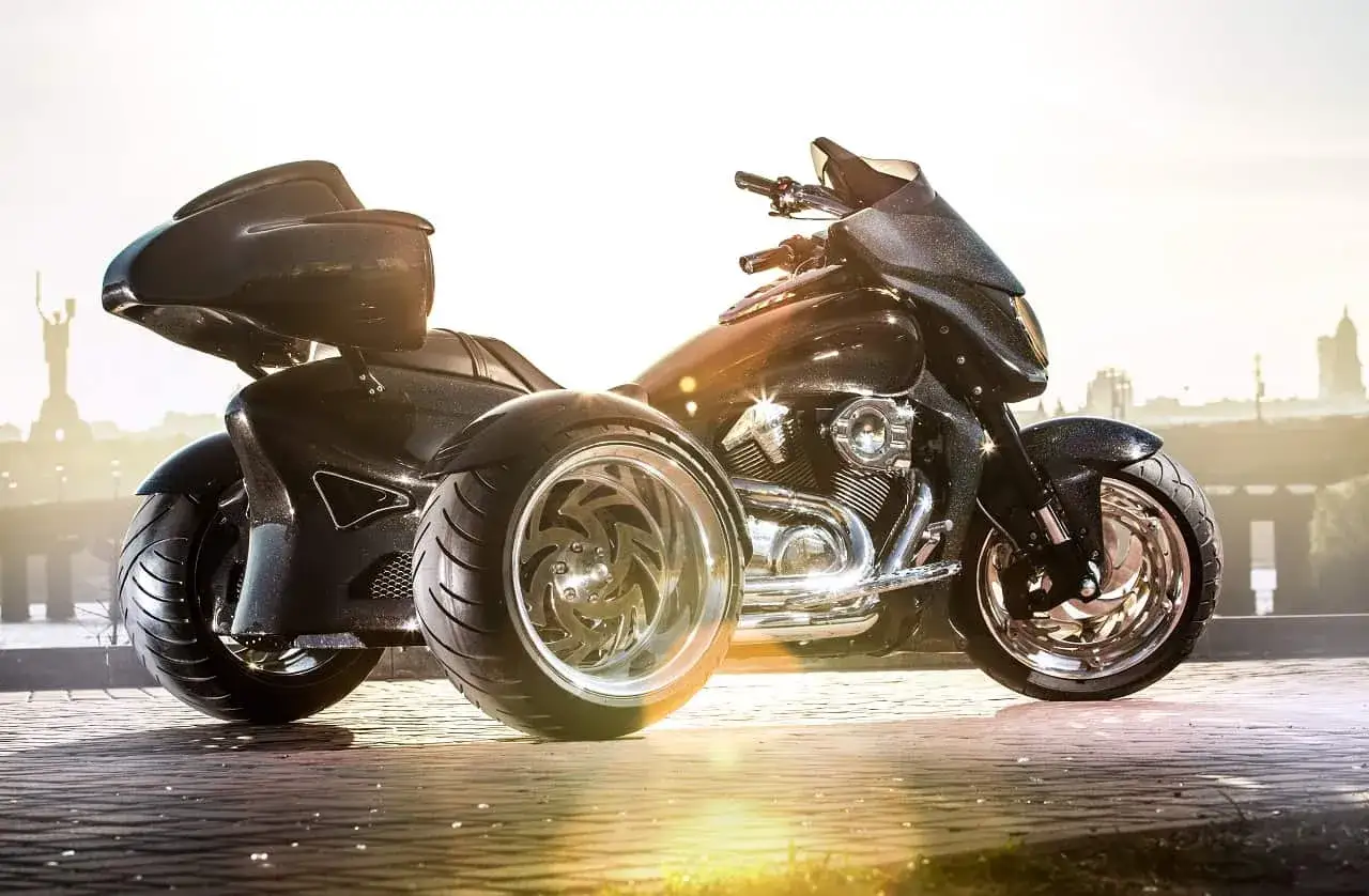 Czarny, lśniący motocykl z dwoma kołami z przodu, z chromowanymi felgami, zaparkowany na bruku.