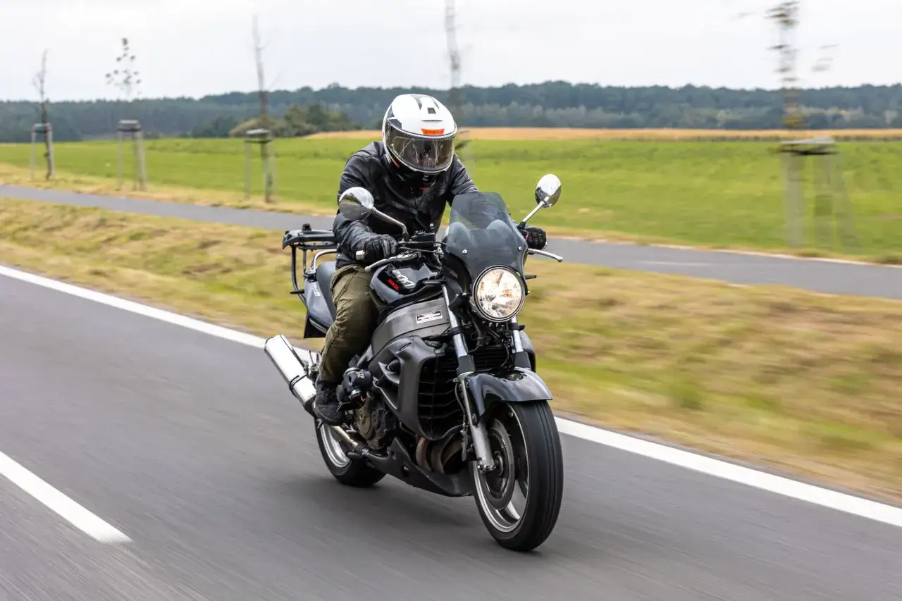 Motocyklista na czarnym motocyklu Honda X11, z widocznymi danymi technicznymi, jedzie po drodze wśród zielonych pól.