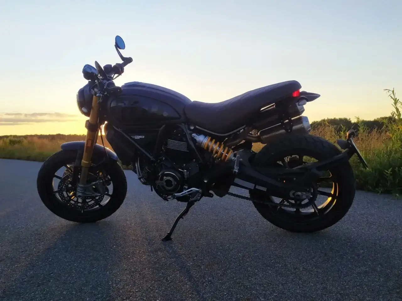 Ciemny Ducati Scrambler 1100 na tle zachodzącego słońca, gotowy na przygodę.