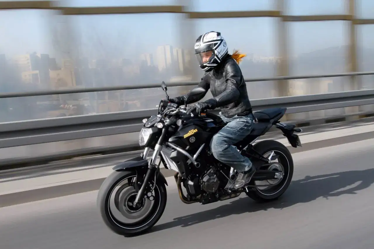Kobieta w kasku i skórzanej kurtce pędzi na czarnym motocyklu Yamaha MT-07. W tle rozmyte miasto.