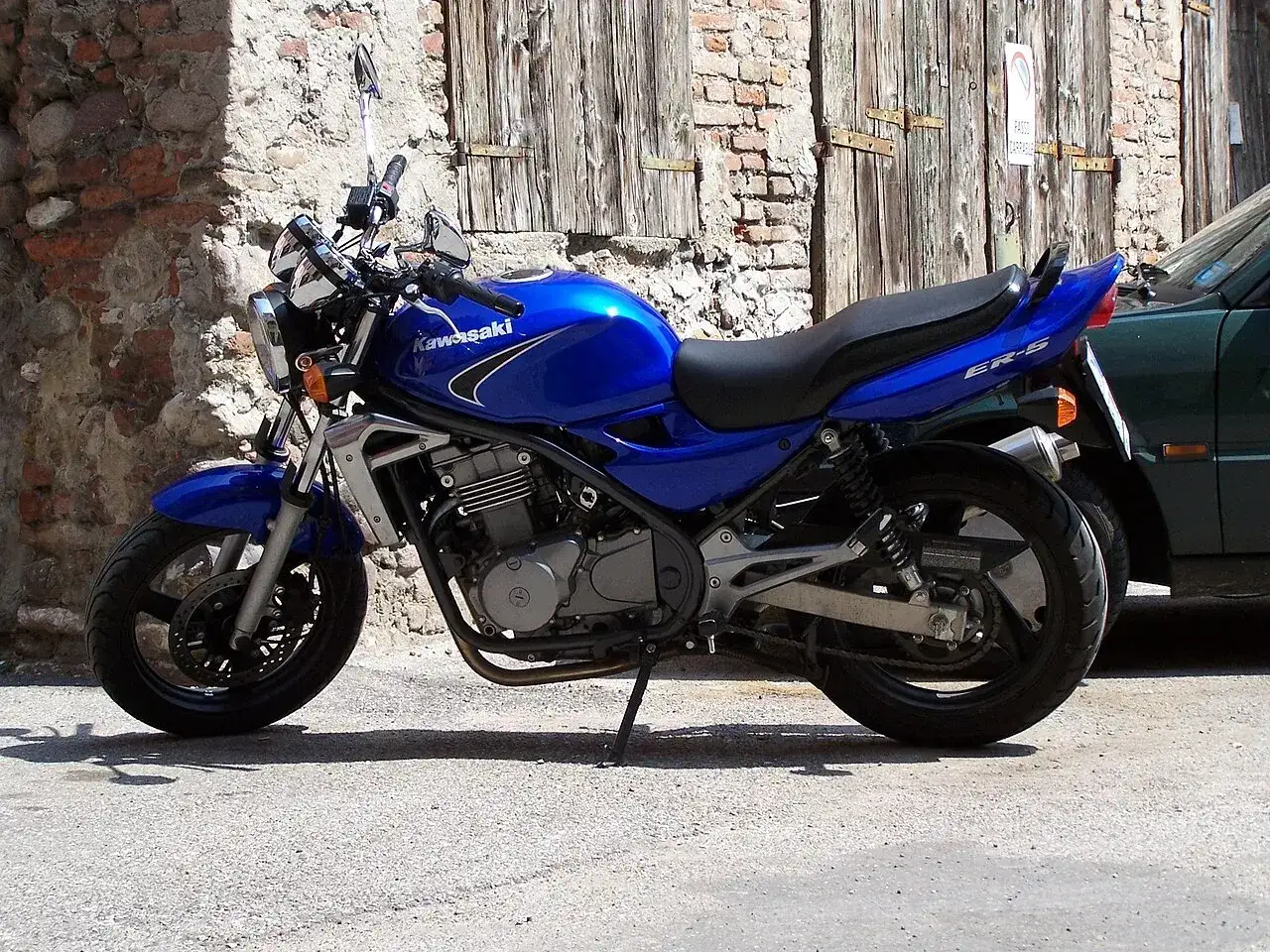 Błękitne Kawasaki ER-5 zaparkowane przy kamiennym murze i drewnianej bramie.