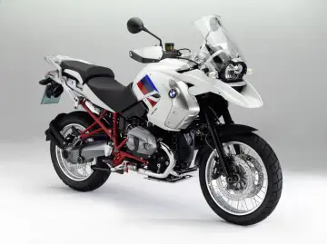 Biały motocykl BMW R1200GS z czerwonym stelażem i flagą na baku. Na co zwrócić uwagę: opony, felgi, silnik, siedzenie, owiewka.