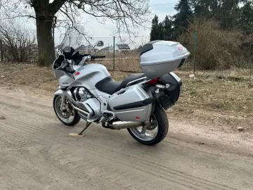 Srebrny motocykl Moto Guzzi Norge z kuframi, gotowy na podróż po wiejskich drogach.